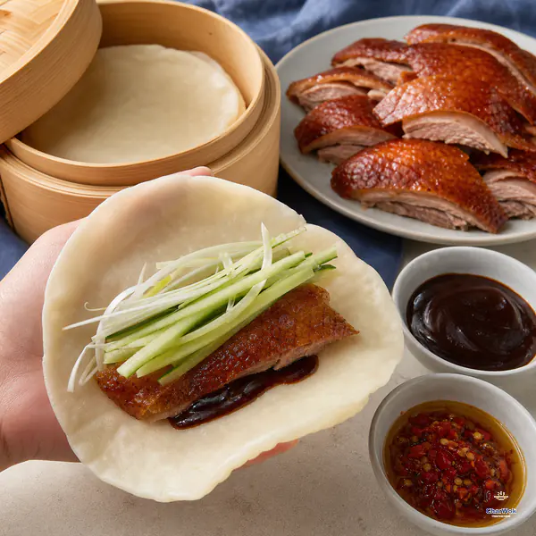 A warm duck pancake holds one piece of crisp duck, cucumber matchsticks, scallion, and a thin smear of dark sauce