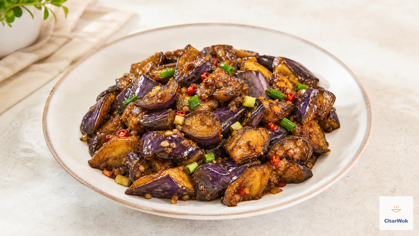 Stir-fried skin-on eggplant chunks coated in a thin glossy reddish-amber plum sauce with scallion greens and fresh red chili