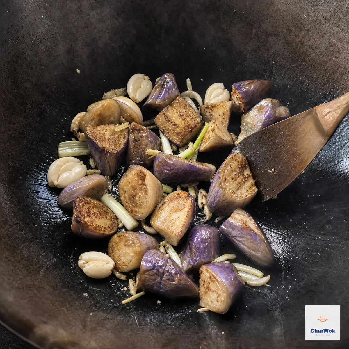 Pre-softened purple eggplant chunks sear with crushed garlic, minced ginger, and scallion whites in a hot carbon-steel wok before the sauce is added