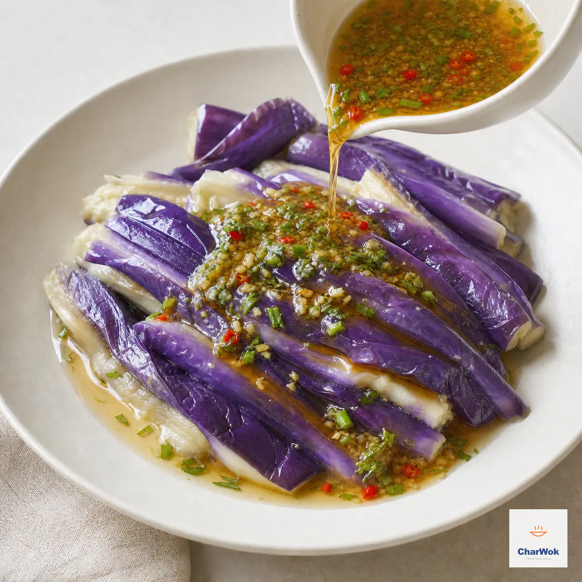 Garlic dressing pours over glossy steamed eggplant strips while their clear steaming liquid remains pooled on the serving plate