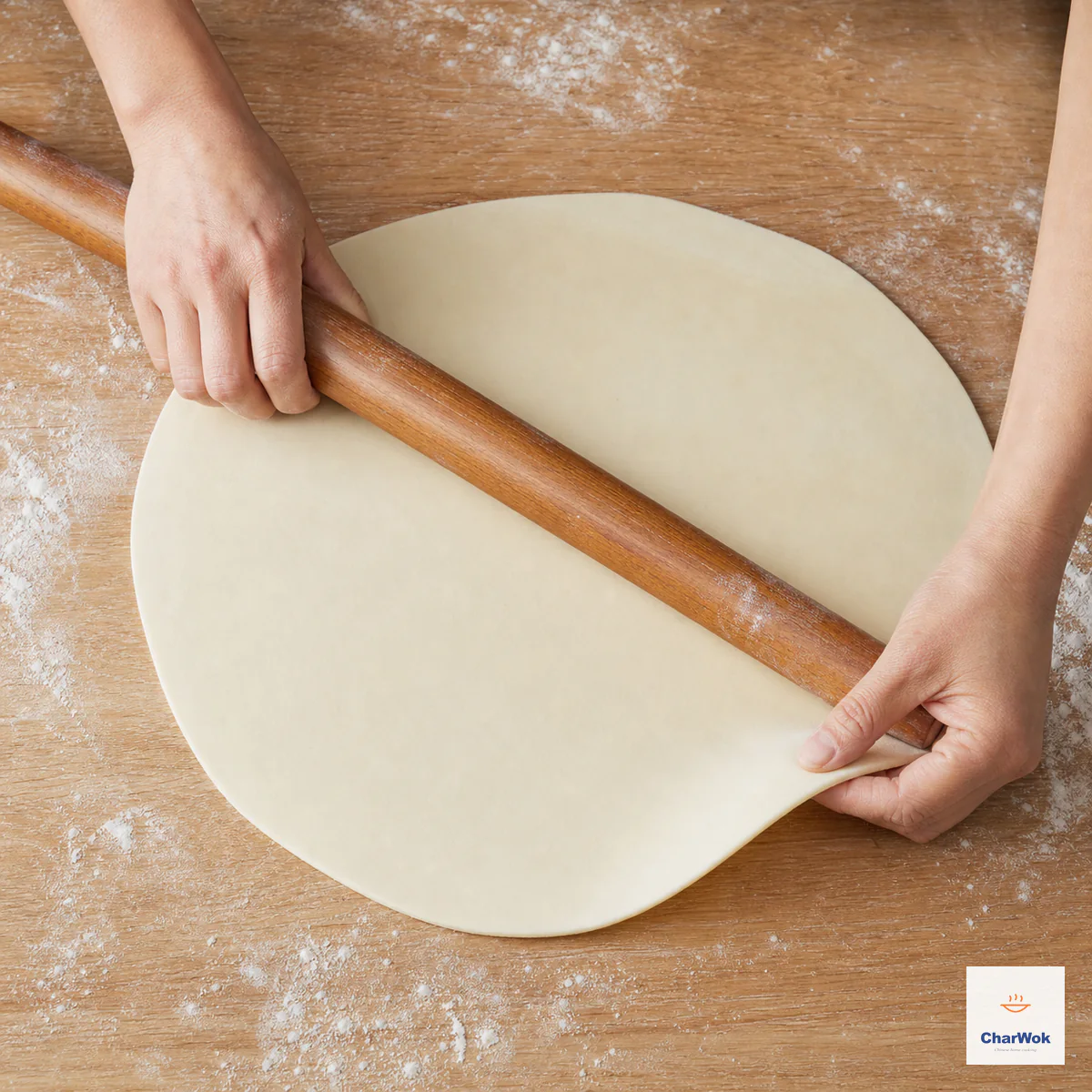 A long rolling pin thins one round noodle sheet evenly while one hand lifts and turns its edge