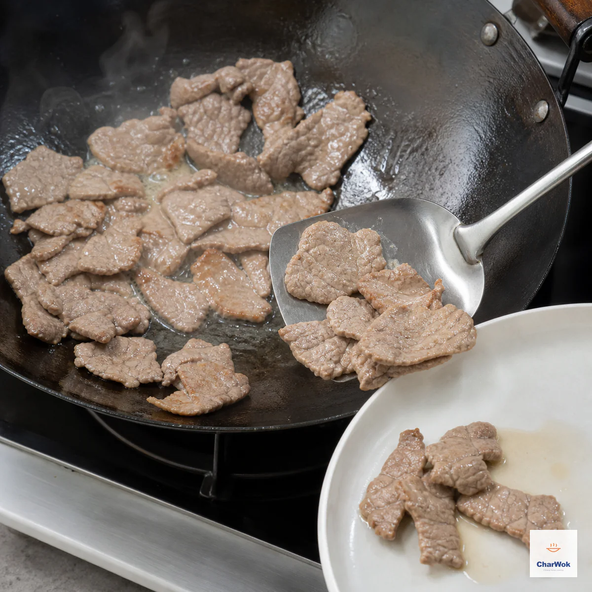 Moist thin beef slices with fully opaque pale-brown surfaces and light caramel patches are lifted from a hot wok onto a white plate