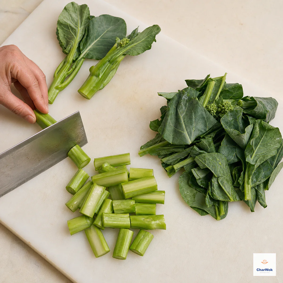 Chinese broccoli is prepared beside a cleaver as one distinct pile of 3 cm split stems and another pile of leafy tops