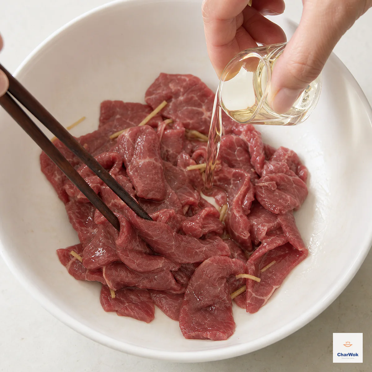 Thin raw beef slices and ginger are turned with chopsticks after the velvet marinade has absorbed while the final oil is added with no liquid pooled below