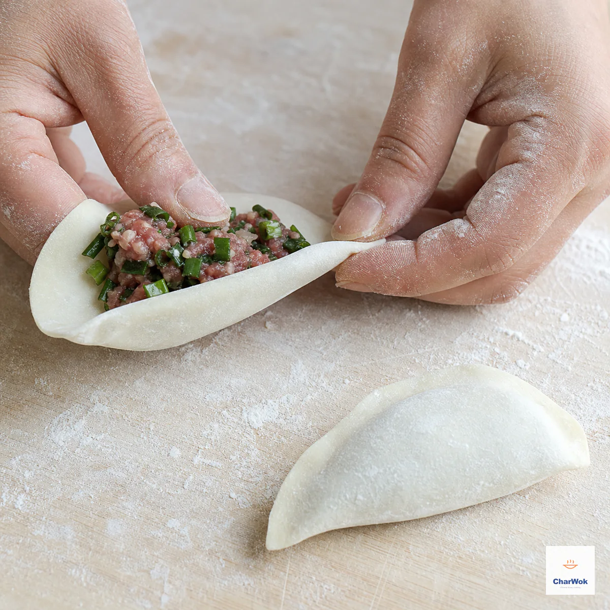 Hands press the final short section of a smooth half-moon dumpling seam closed over a modest amount of raw beef-and-chive filling