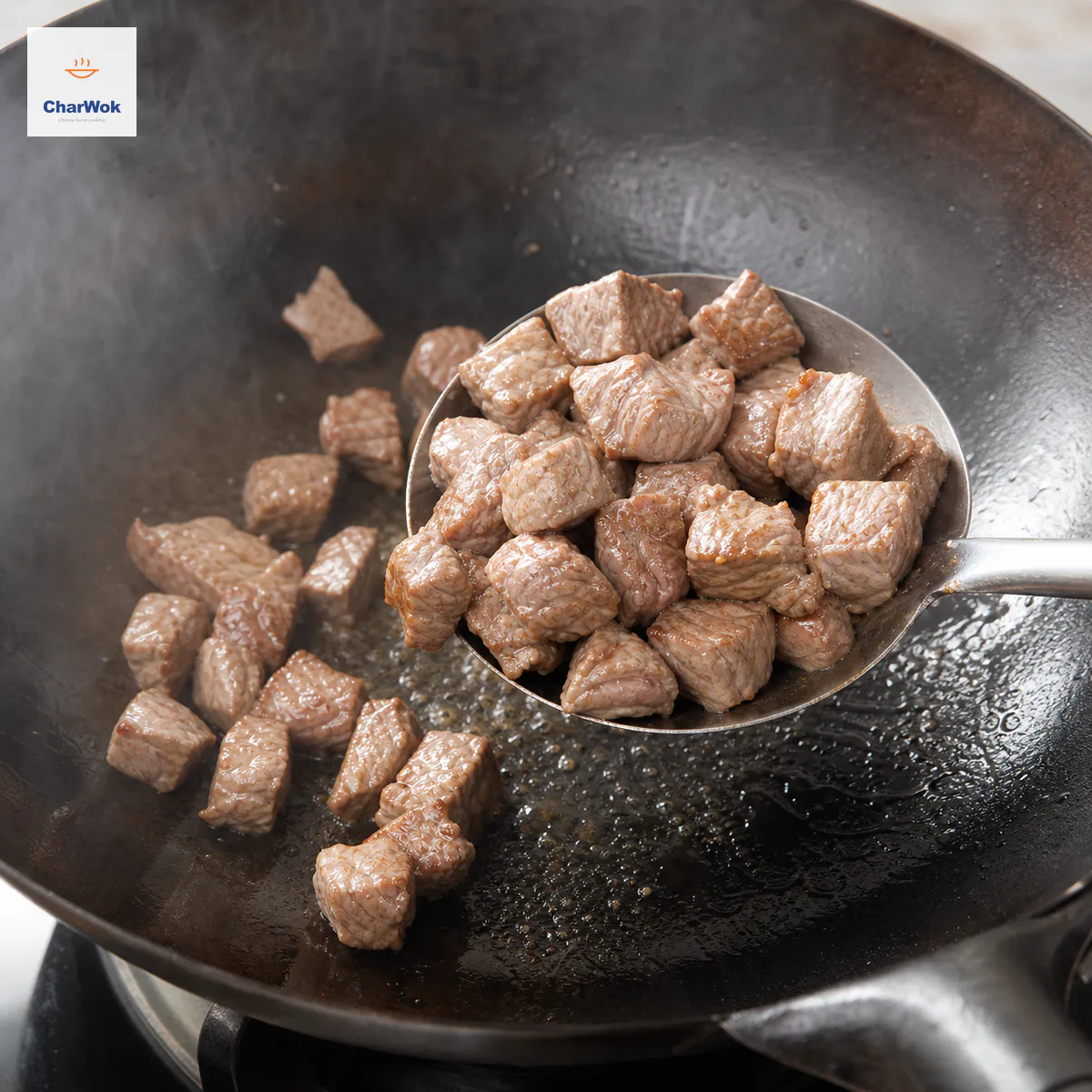 A wok spatula lifts lightly colored beef dice whose visible surfaces have just lost all raw red while a thin sheen of oil remains in the smoking wok