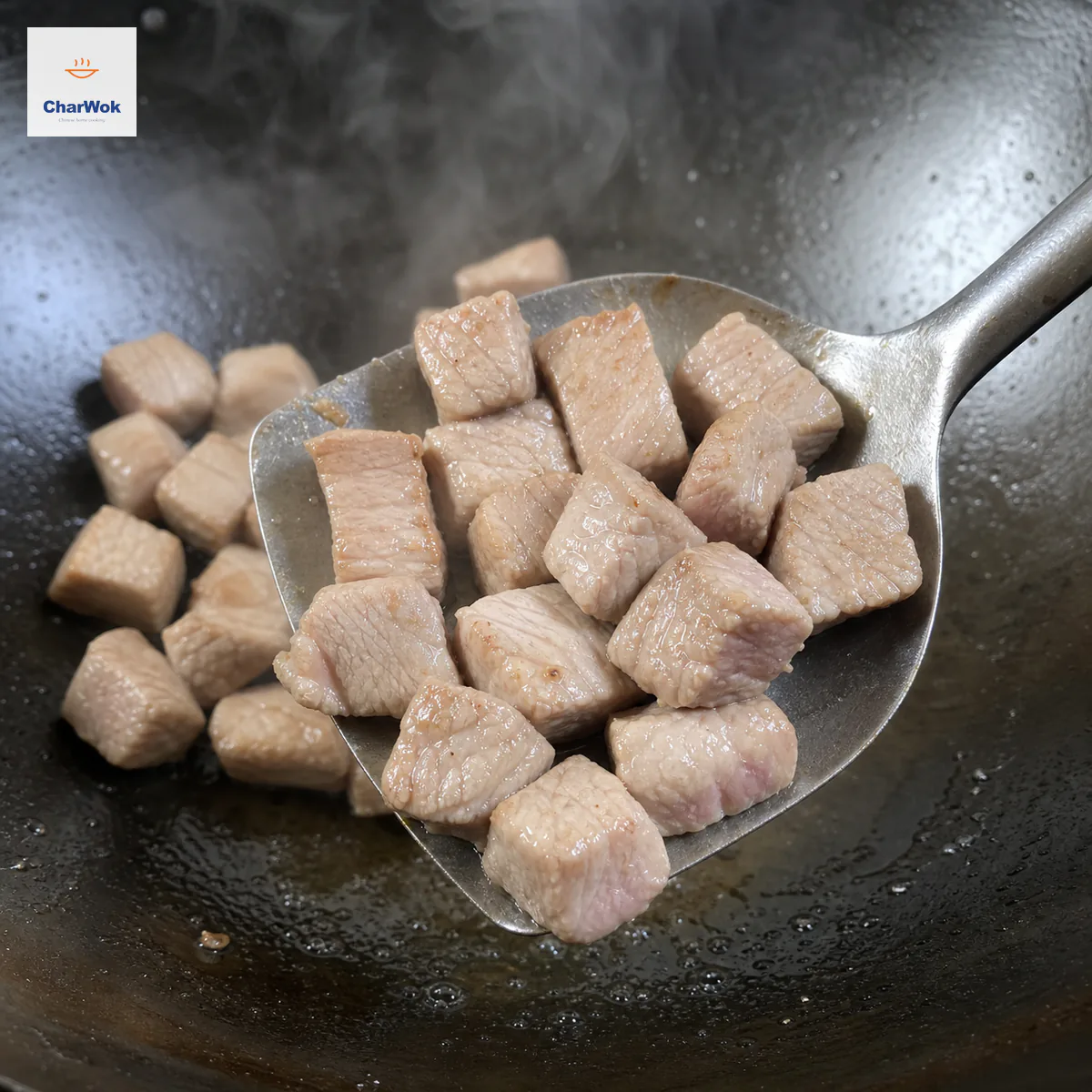 锅铲正从冒烟炒锅盛起牛肉丁，多数外表已转粉白，只有两三处边缘仍微微透粉红，锅中只留薄油