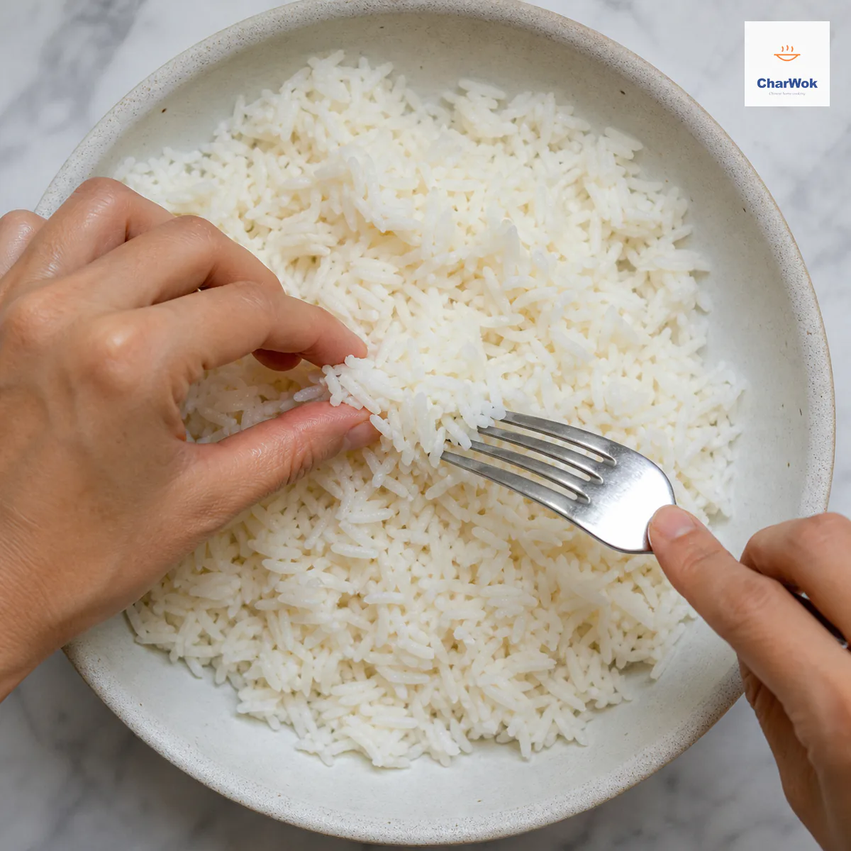 Damp fingertips and a fork separate the final small clump of cold jasmine rice while the rest of the firm grains already lie loose with no pooled water