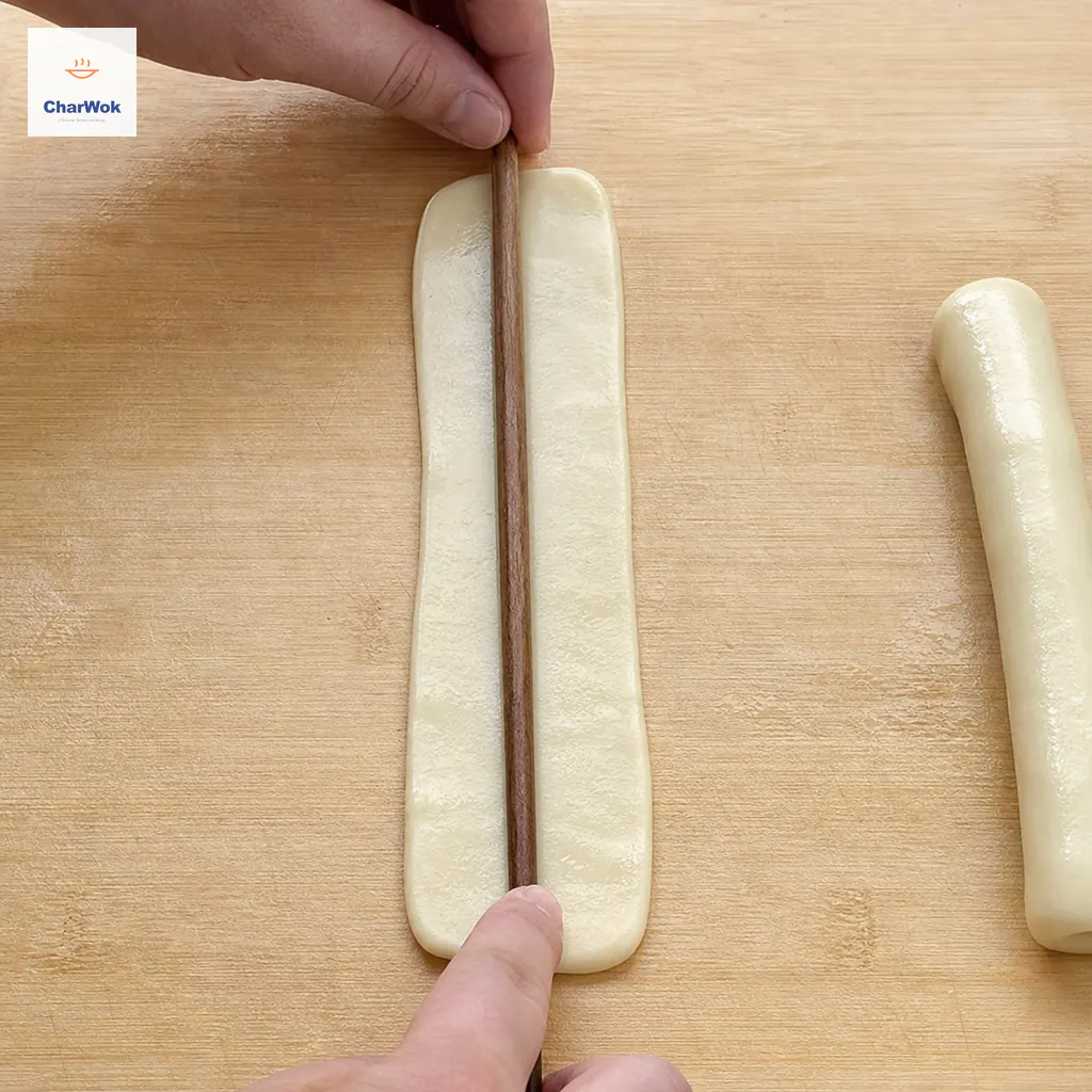 A wooden chopstick presses a continuous shallow center groove into one neat oiled dough rectangle without cutting through it
