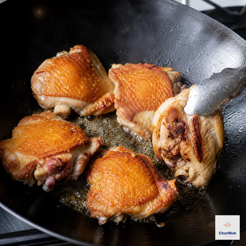 Large bone-in skin-on chicken-thigh pieces sear in one uncrowded wok layer with deeply golden crisp skin while tongs turn one piece to show browned contact marks