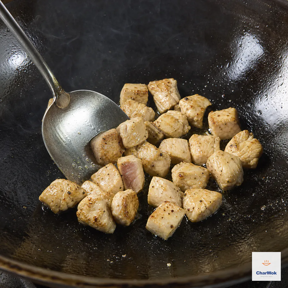 Chicken thigh cubes receive a brief first sear in one uncrowded wok layer while an instant-read thermometer waits beside the pan for the final temperature check