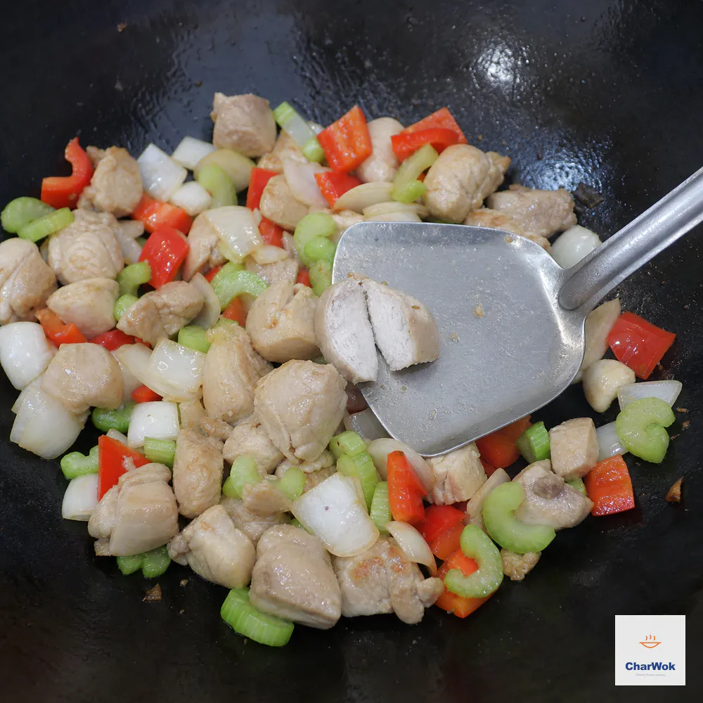 Chicken cubes, diced onion, red bell pepper, and celery are tossed in a hot wok while an instant-read thermometer in a thick chicken cube reads 165°F (74°C)