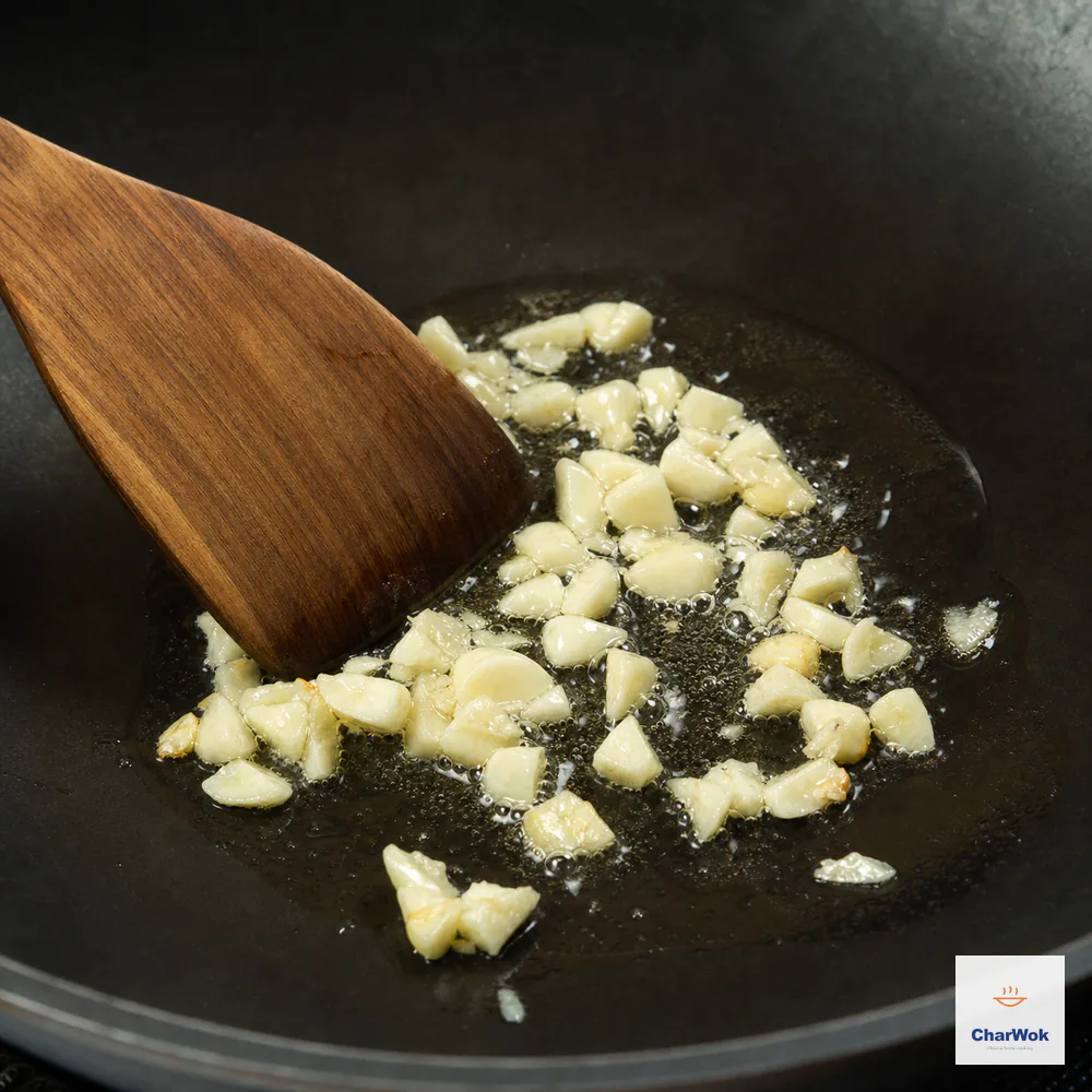 Coarsely chopped garlic gently sizzles in a shallow film of warm neutral oil with most pieces ivory and only a few edges beginning to turn pale gold
