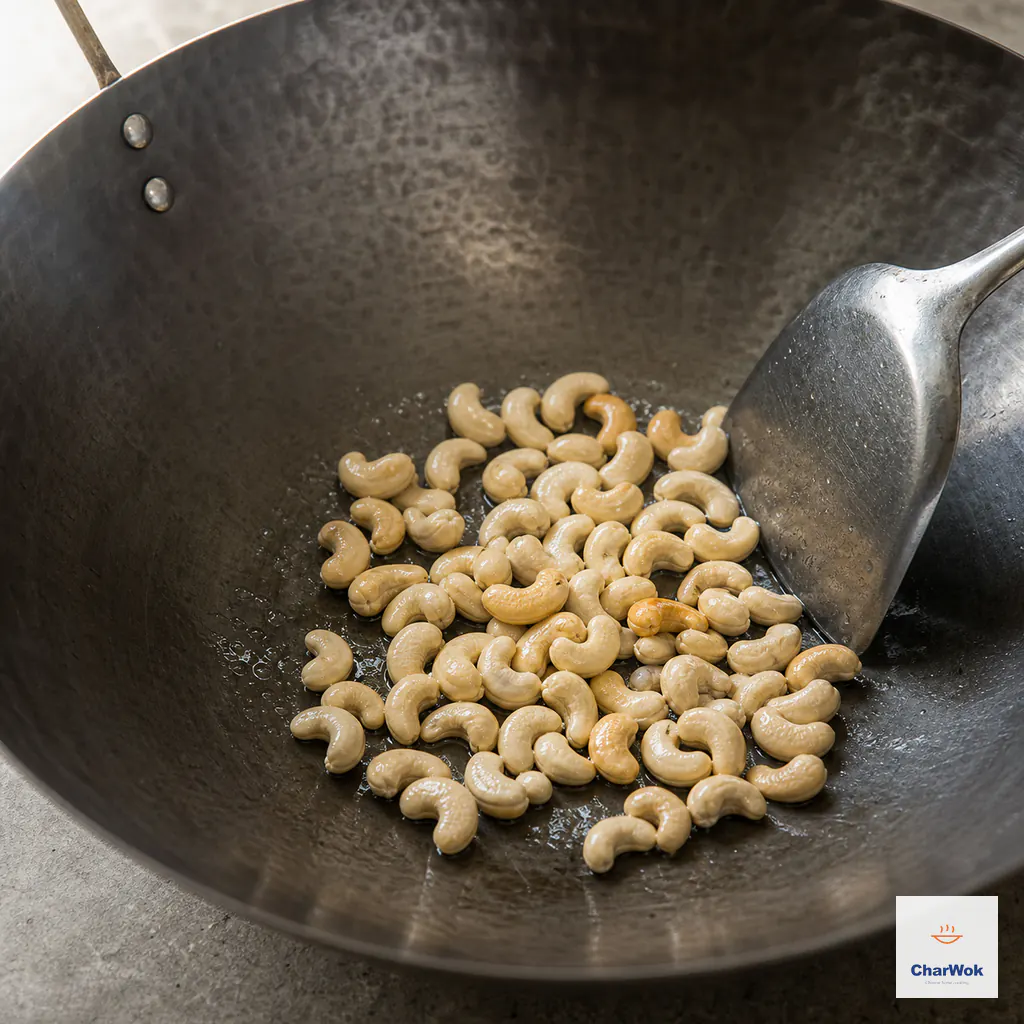 Raw cashews fry in a thin film of oil in a carbon-steel wok, with most still cream-colored and a few just turning pale gold