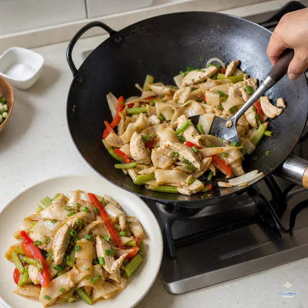 Freshly chopped scallions are tossed through intact wide rice noodles, moist chicken, red pepper, onion, and celery as the first portion is transferred to an ivory plate