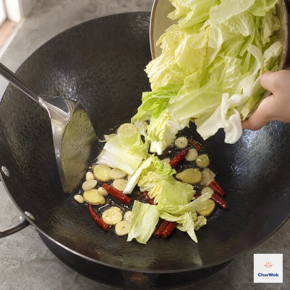 Raw bulky hand-torn cabbage falls into a hot wok over pale-gold garlic slices, ginger coins, and six dried red chillies