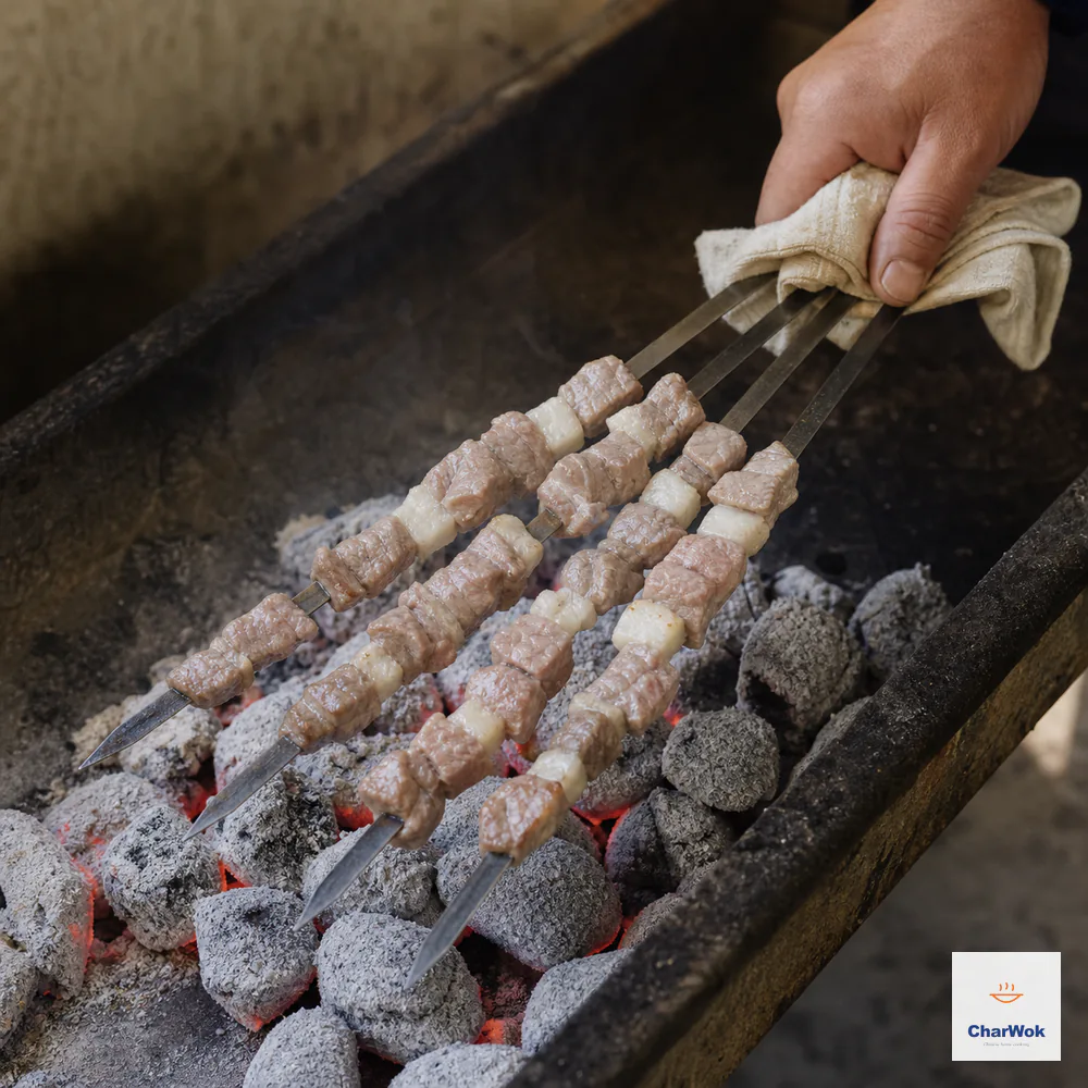 A hand turns unseasoned lamb skewers close above white-ash charcoal after the meat surface has changed from raw red to pale, with no open flame