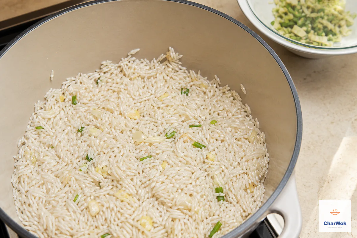 Thoroughly drained raw jasmine-rice grains are stirred through the small amount of scallion, ginger and garlic left in the pot