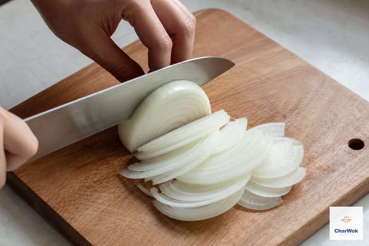 A yellow onion is cut into thin, even half-moon slices on a wooden cutting board