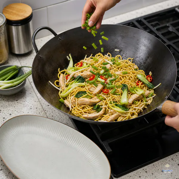 Fresh green scallion slices are scattered over dry glossy chicken chow mein beside an empty serving platter