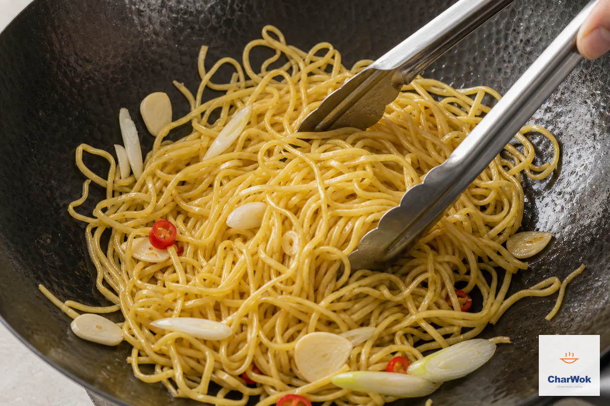 Loose yellow egg noodles fry with white scallion pieces, red chili rings and sliced garlic that remains pale and uncolored