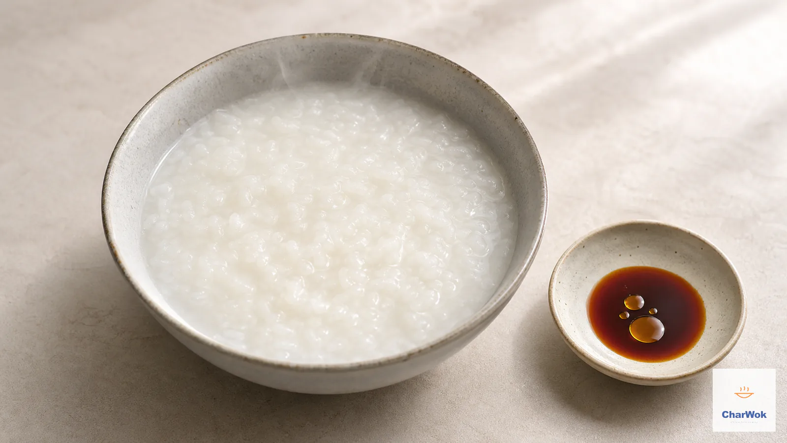 Steaming plain white congee with softened rice grains beside soy sauce and toasted sesame oil