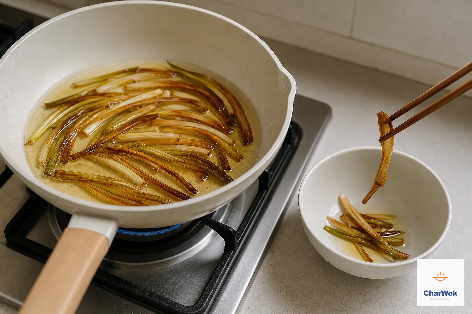 Deep-amber scallion sections infuse clear golden oil over a tiny blue flame while chopsticks lift one almost-crisp strip before it blackens