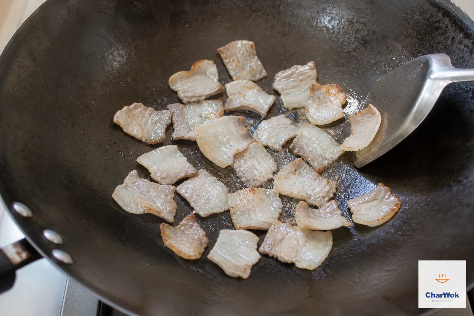 Thin pork-belly slices render in one uncrowded layer with curled pale-golden edges and a thin film of fat in the wok