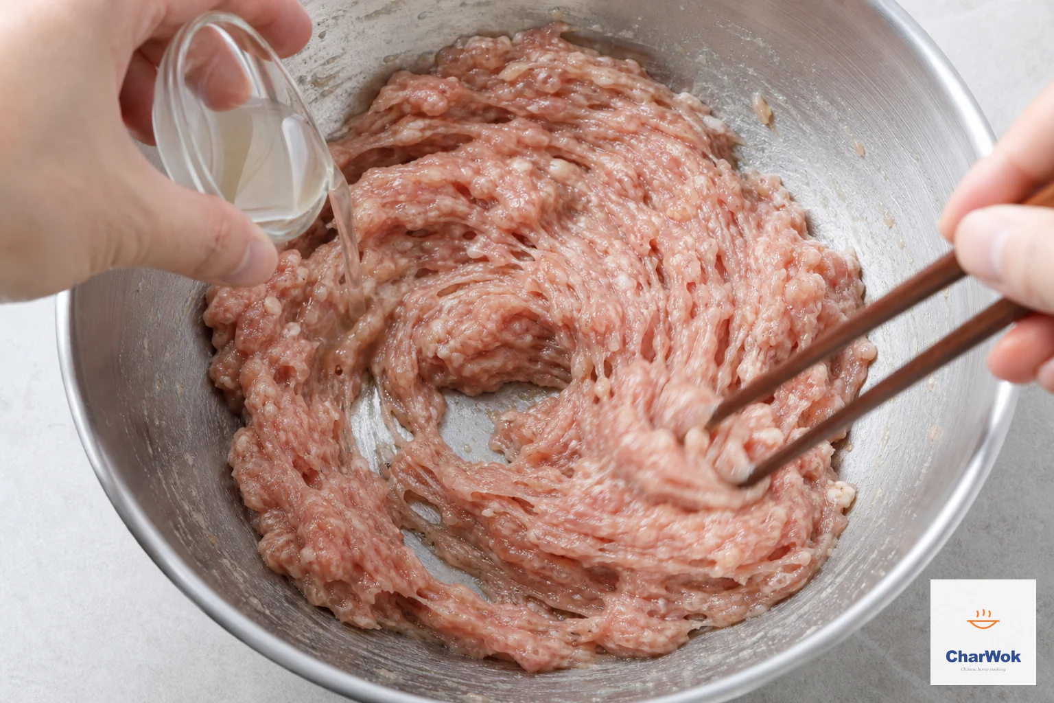 A small measure of clear stock pours into glossy pork while chopsticks beat it in one direction and the bowl bottom remains free of liquid