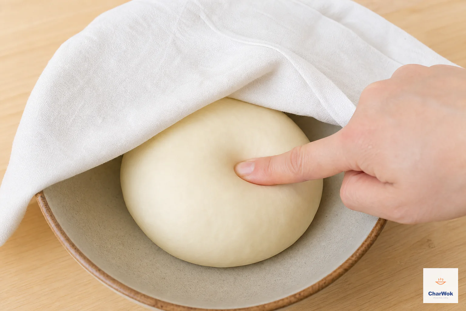 A smooth unrisen dumpling dough ball rests under a damp cloth with a shallow fingertip indentation showing relaxed gluten