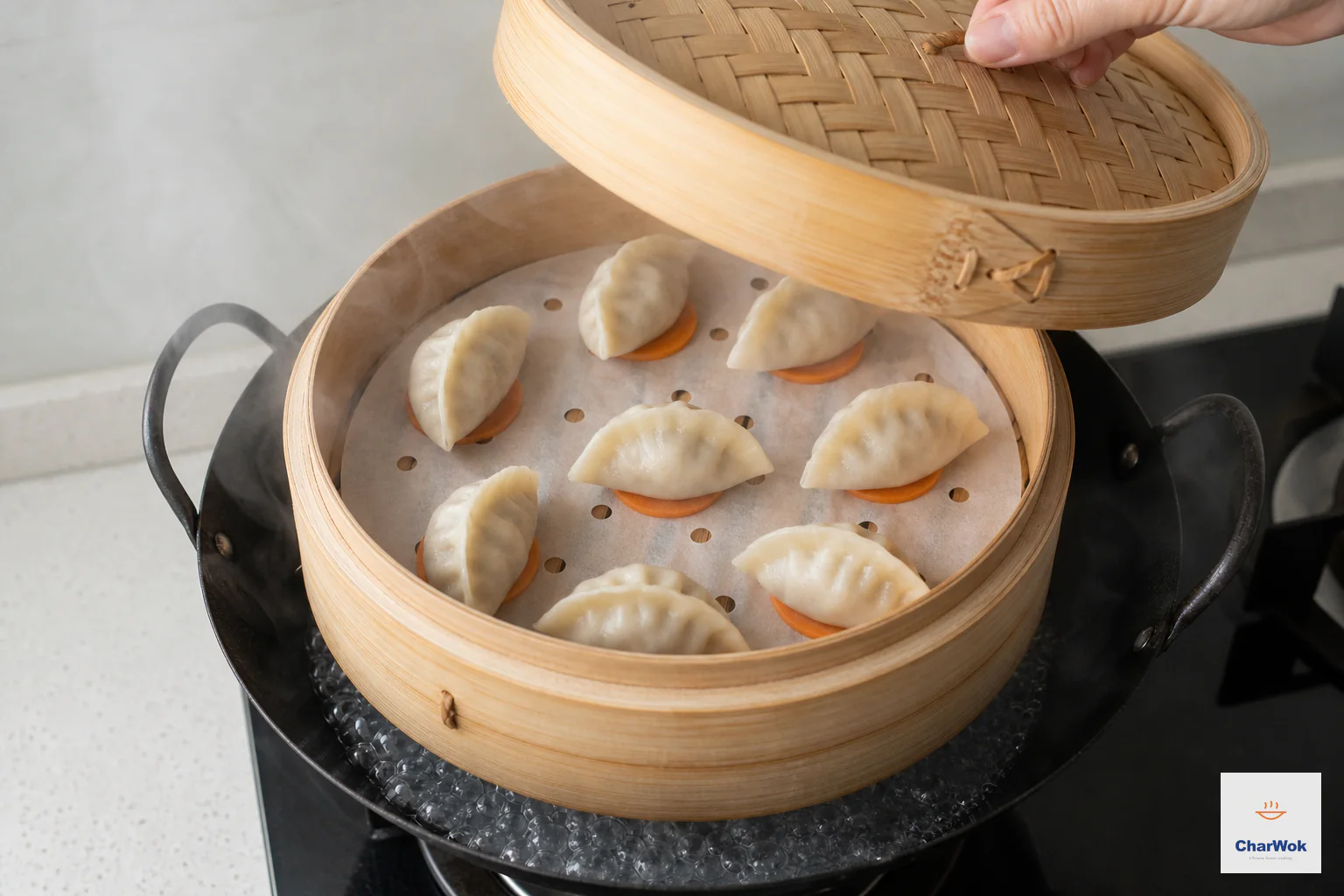 Raw dumplings sit well spaced in a bamboo steamer lined with perforated parchment and carrot slices above actively boiling water
