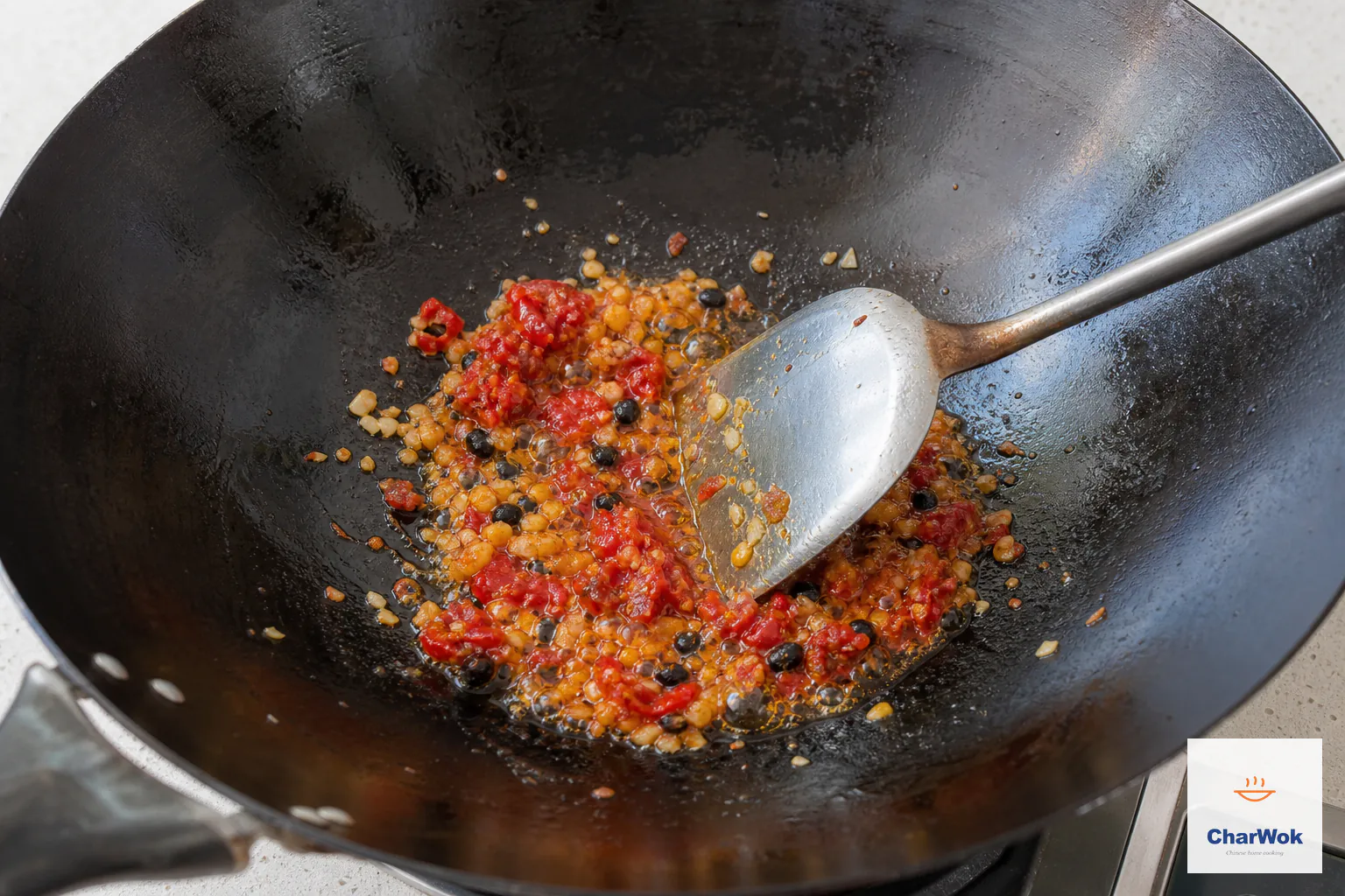 Coarse red duo jiao, pale minced garlic and wrinkled black fermented beans sizzle in orange-red oil in a dark wok