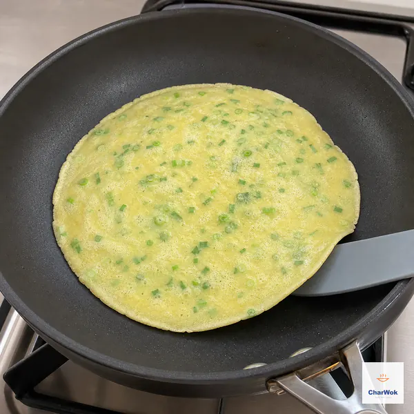 A thin egg-and-scallion crepe with a matte set surface and slightly curled edge slides freely as a spatula slips underneath