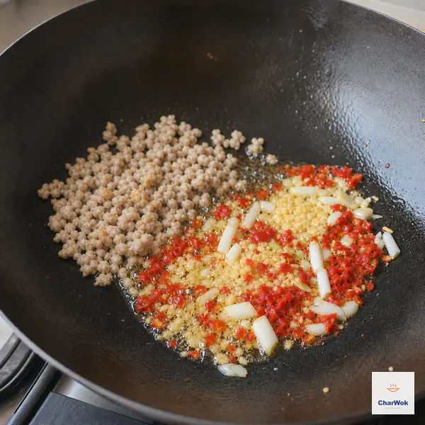 Chopped pickled chili, minced garlic, ginger, and scallion whites bloom beside cooked ground-pork crumbles in a wok