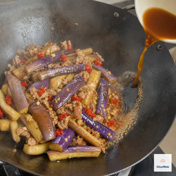 Smooth amber sauce is poured around the hot wok rim over intact eggplant, ground pork, and chopped pickled chili