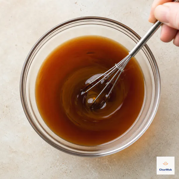 A small whisk thoroughly re-stirs smooth translucent amber sauce with no cornstarch sediment visible
