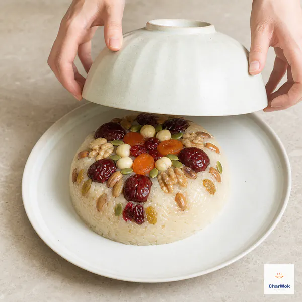 Two hands lift an inverted bowl straight up to reveal an intact sticky-rice dome with the treasure pattern face-up
