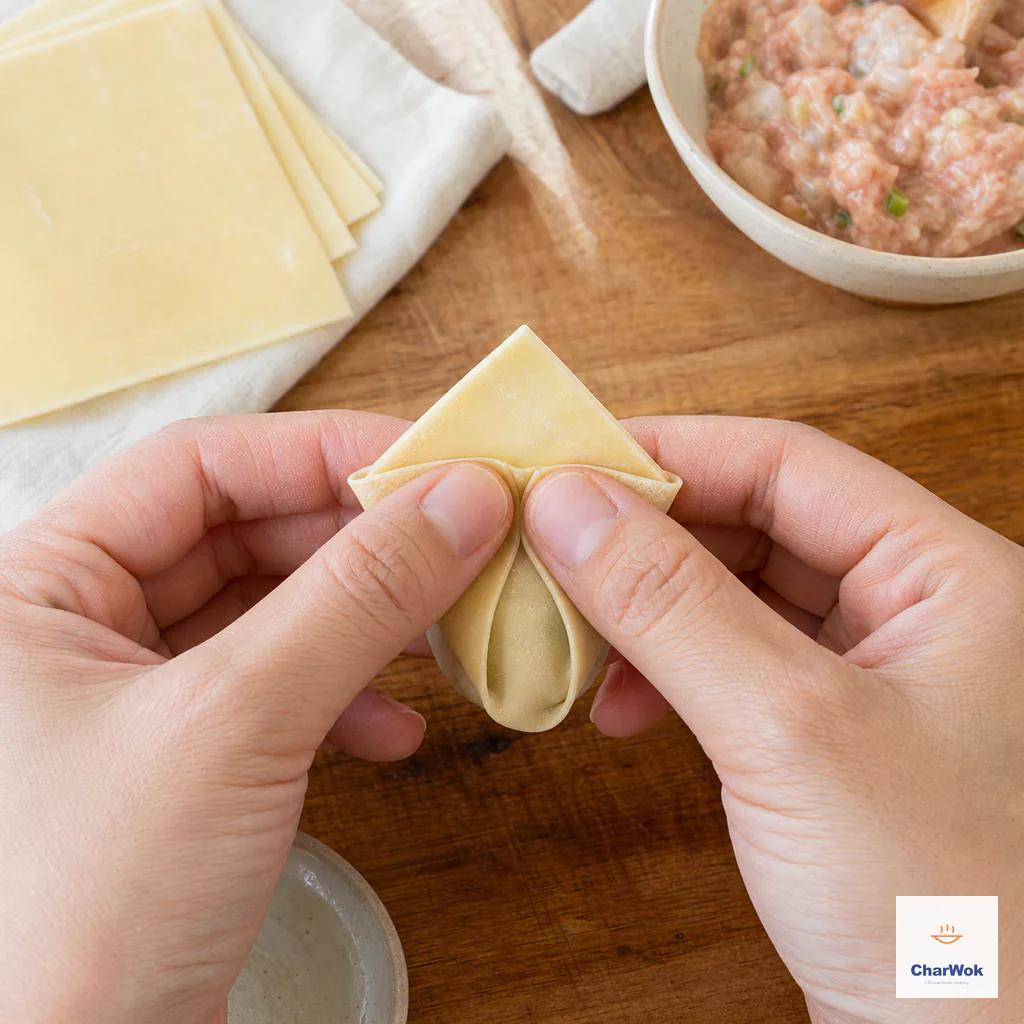 Two side corners overlap over a visible top corner and are pinched into a bishop-hat wonton