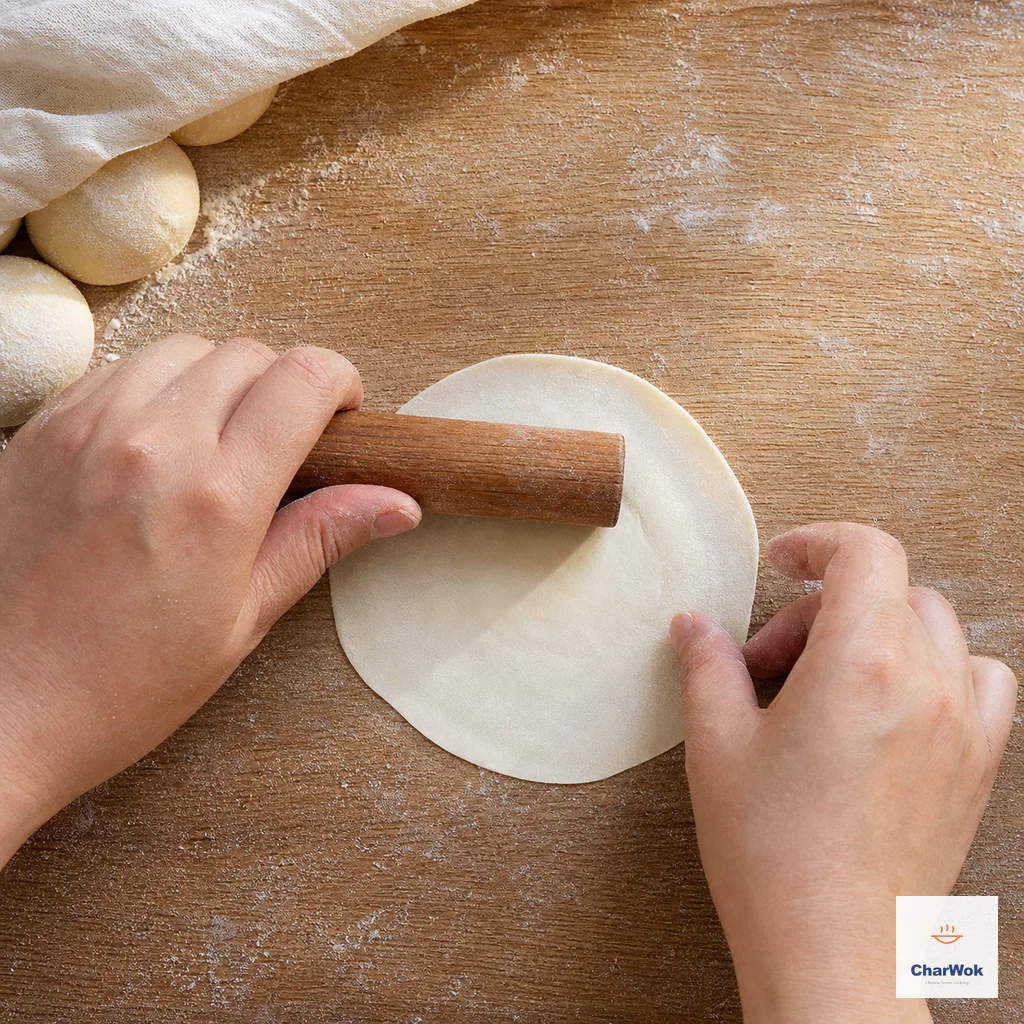A short rolling pin travels halfway across a round dough disc while the other hand rotates its thin rim