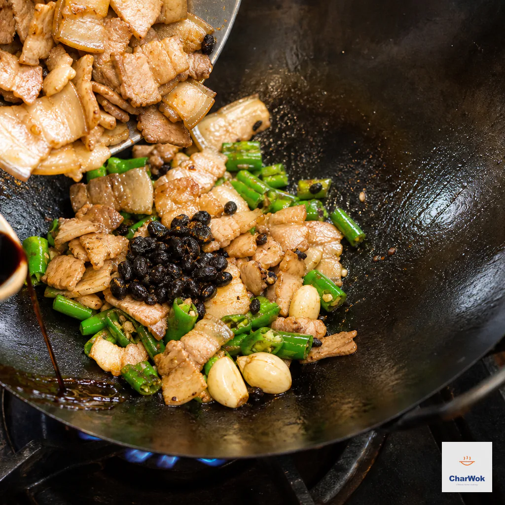 Browned pork returns to blistered green chilies as fermented black beans are added and soy sauce runs down the exposed hot wok wall