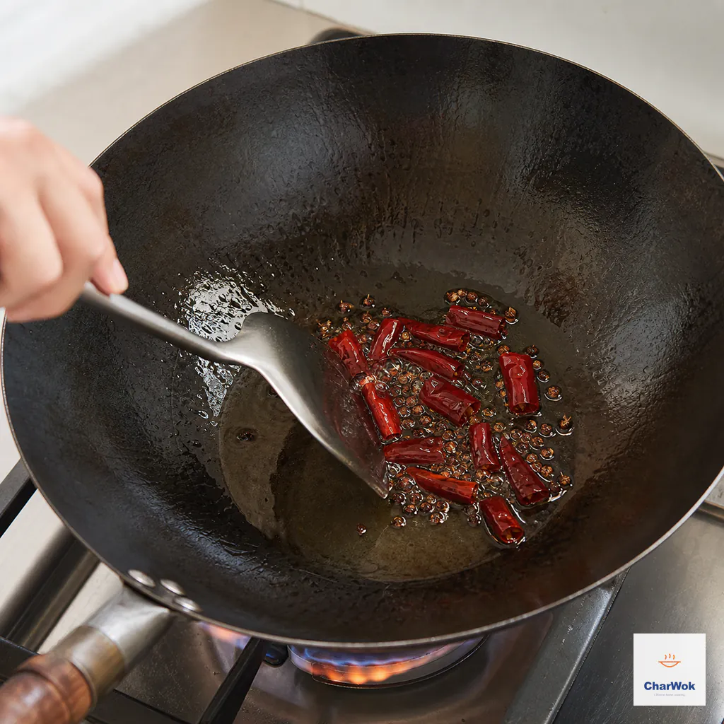Deep-red dried chili segments and whole Sichuan peppercorns bubble briefly in a thin film of oil while a wok spatula keeps them moving