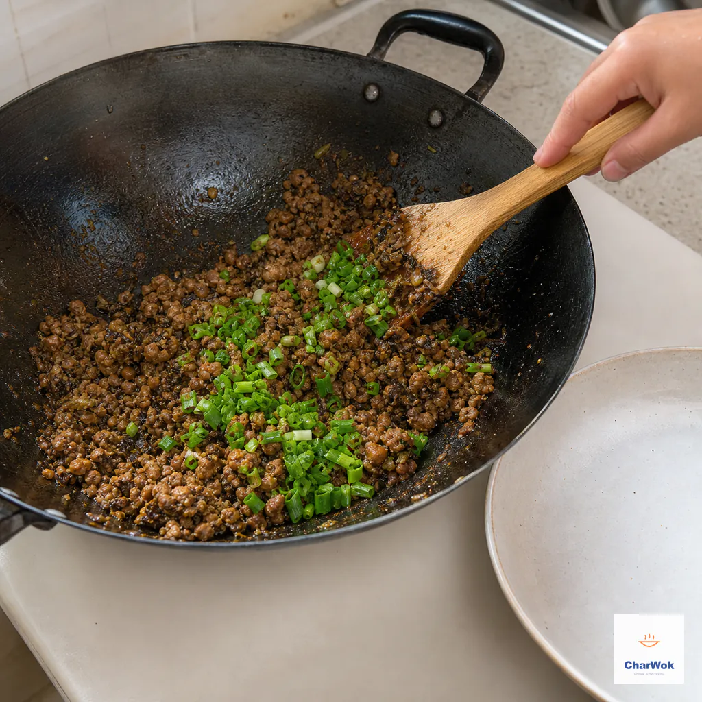 Cooked minced pork and Ya Cai have no pink or pooled liquid as fresh scallion is folded in over an extinguished burner beside a waiting cooling plate