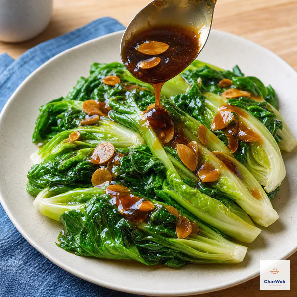 A spoon pours thick glossy oyster sauce and pale-gold garlic slices over drained bright-green lettuce