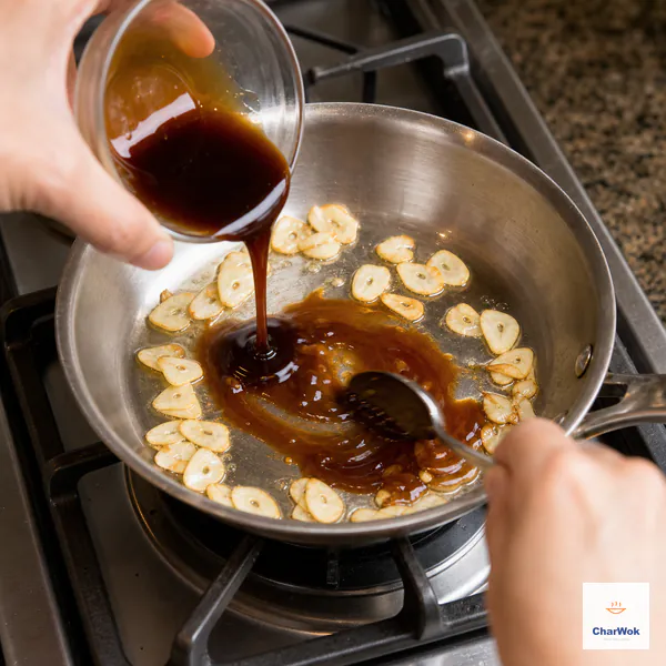 Prepared brown sauce is poured around pale-gold garlic slices in a skillet over an unlit burner while a spoon stirs