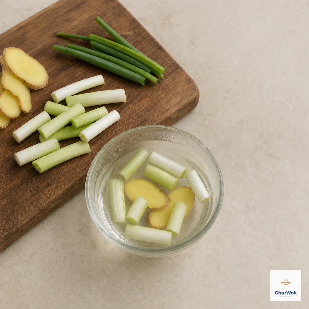 Scallion sections and ginger slices steep in a small bowl of warm water beside reserved scallion-green tops