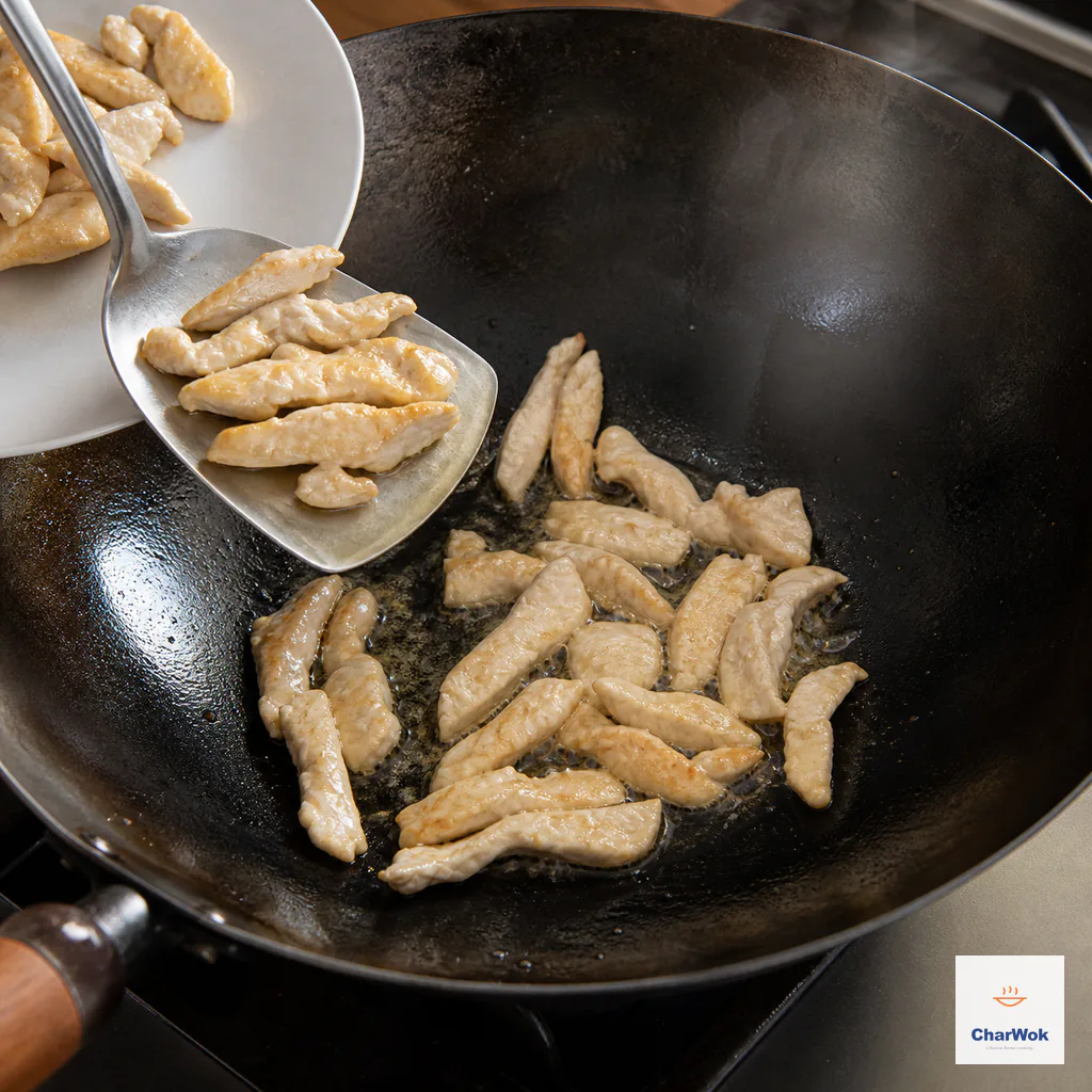Pale-golden chicken strips are lifted from a hot carbon-steel wok onto a clean plain plate after the coating sets