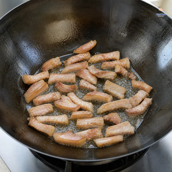 Pinky-width strips of skin-on pork belly brown in a dry carbon-steel wok above a shallow pool of clear rendered fat