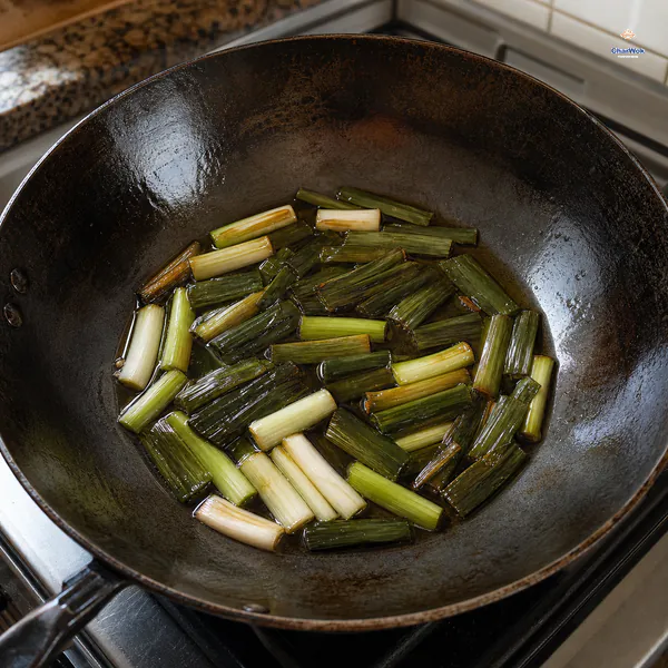 Scallion whites and deep-olive green segments sit in clear golden oil with the first light-brown edges and no flame under the wok