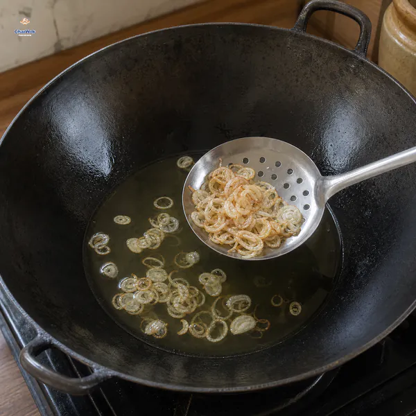 A slotted spoon lifts translucent pale-gold shallot rings from an almost still pool of clear oil in a dark wok