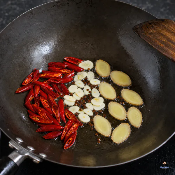 Eight ginger slices, thin garlic slices, Sichuan peppercorns and halved seeded dried chilies bloom in a shallow sheen of oil in a dark wok